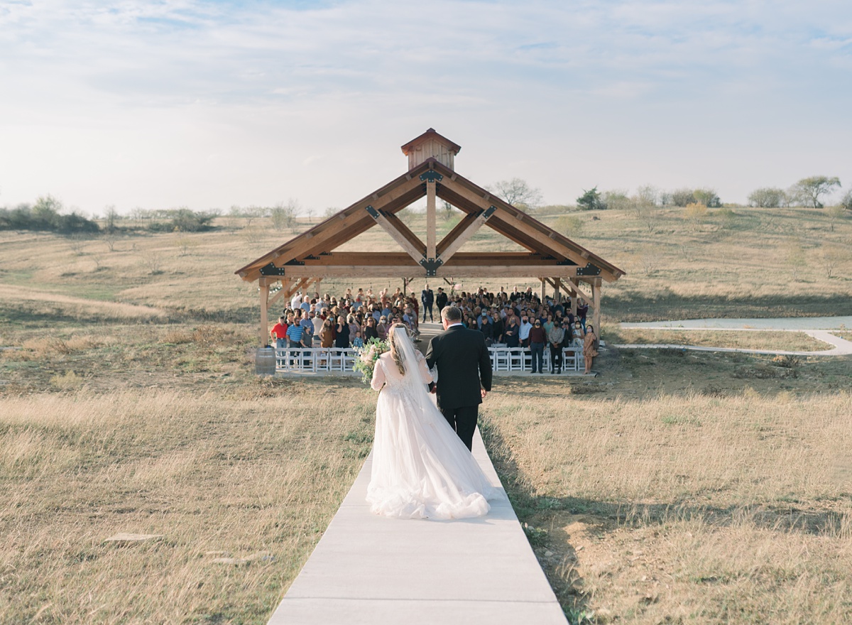 bride from behind walking down aisle - Blue Hills Ranch Fall wedding near Waco, TX