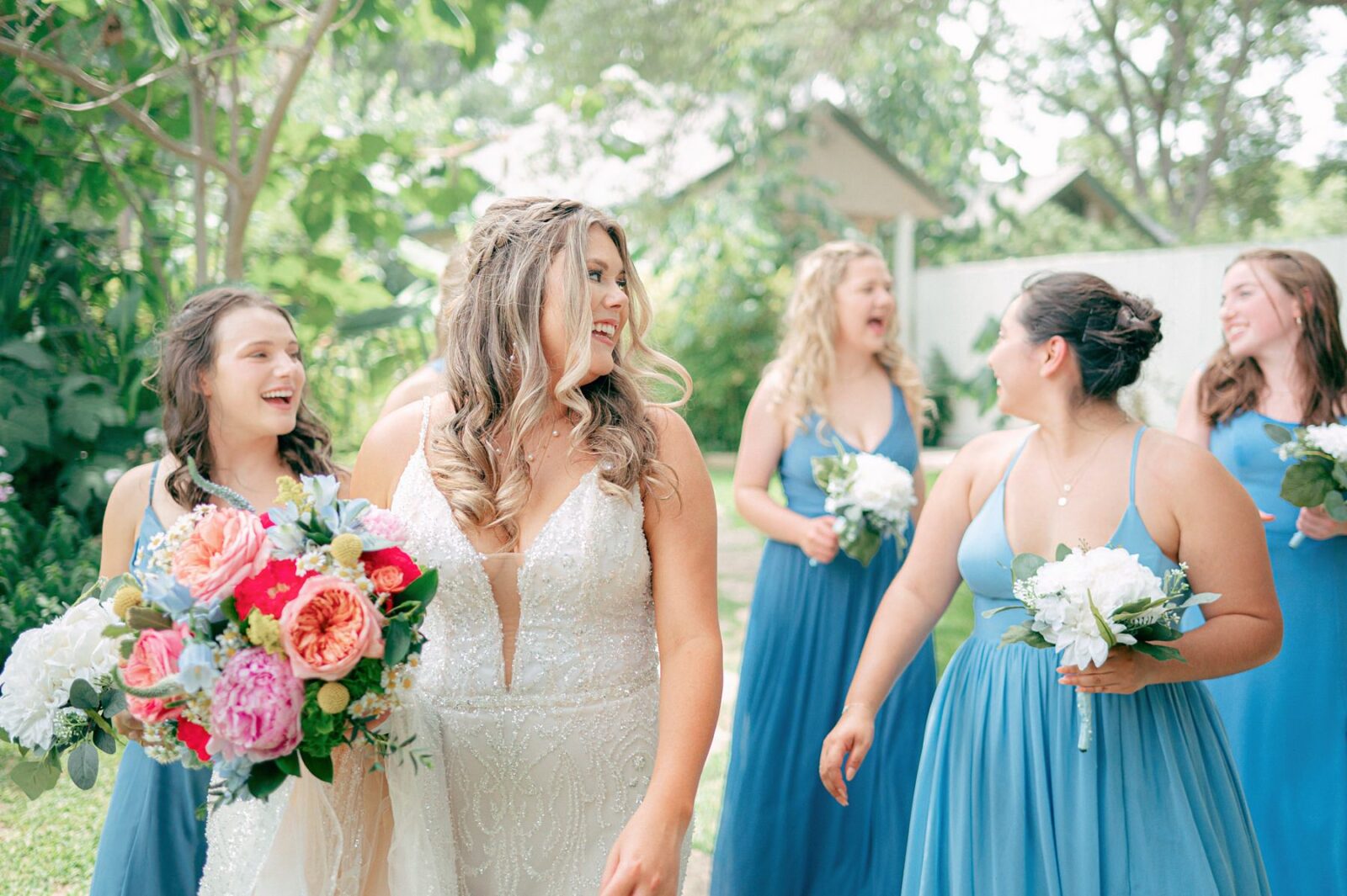 bride looking back at her bridesmaids, blue bridesmaid dresses, Austin Wedding at Hummingbird House, with wedding photos by Tara Lyons Photography. Other vendors: Mistique Makeup, Cana Events, Twin Flame Events, Simply Chic Event Rentals, Live Oak Photo Booth