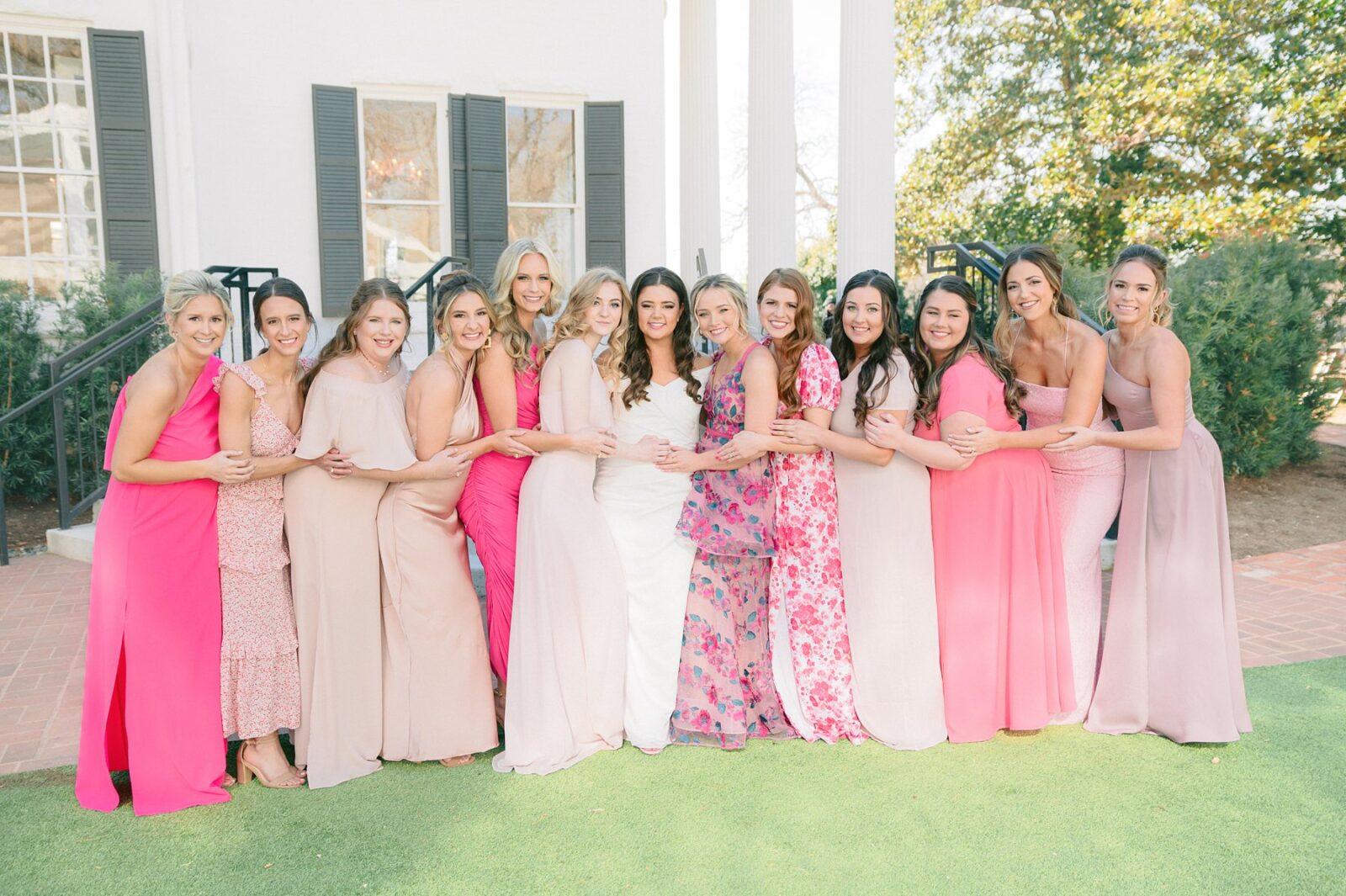 coordinating pink bridesmaid dresses, mismatched pink bridesmaid dresses, pink wedding decor, large wedding party, twelve bridesmaids, large wedding party posing ideas, wedding at Woodbine mansion in round rock texas, wedding photos by Tara Lyons Photography, planning by The event shop